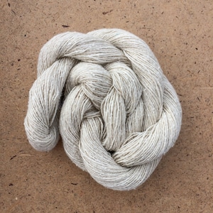 May include: A skein of natural white yarn, made from a blend of cotton and linen, is tightly wound into a circular shape.