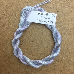 Puede incluir: Una madeja de hilo de seda hilada de color azul claro, morado y blanco. La etiqueta dice "Spun Silk 16/2, 20 metros, Colour No. S 28".