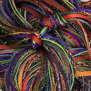 May include: A close-up of a bundle of colorful embroidery floss in shades of red, orange, green, purple, and gold. The floss is arranged in a tangled, interwoven pattern.