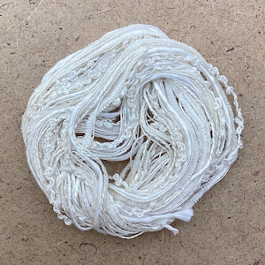 Könnte beinhalten: Nahaufnahme eines weißen Garnknäuels aus verschiedenen Texturen und Stärken. Das Garn ist locker gewickelt und wirkt weich und zart.