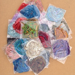 May include: Assortment of colorful embroidery floss spools in individual clear plastic bags. The floss is arranged in a pile, with the bags overlapping.