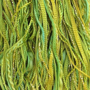 Puede incluir: Primer plano de un manojo de hilo verde, amarillo y plateado. El hilo está dispuesto en un patrón aleatorio, creando una visualización texturizada y colorida.