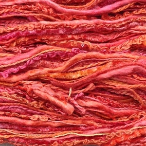 May include: Close-up of a bundle of colourful yarn in shades of orange, pink, and red. The yarn is made of a variety of textures, including smooth, fuzzy, and textured strands.