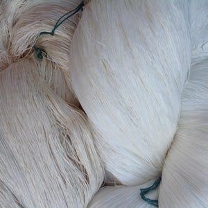 May include: A close-up of a pile of white yarn, with some green string visible.