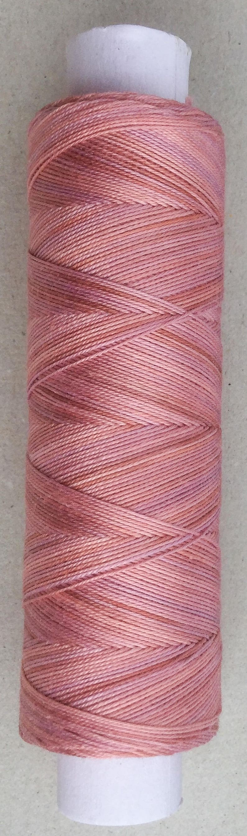 May include: A spool of pink and peach colored thread wound around a white cardboard tube.