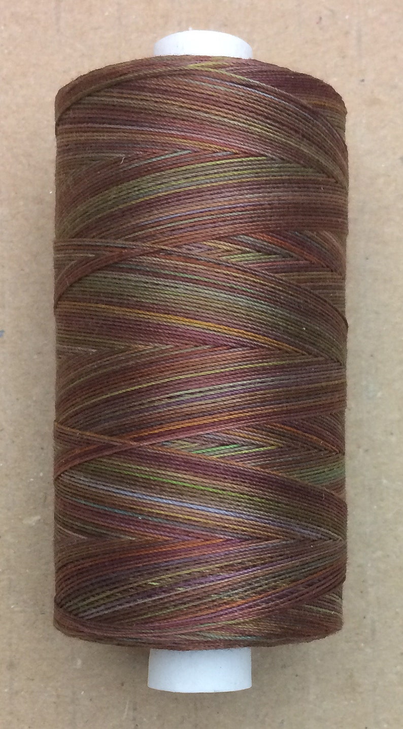May include: A spool of multi-colored thread with shades of brown, green, purple, and orange. The thread is wound around a white plastic bobbin.