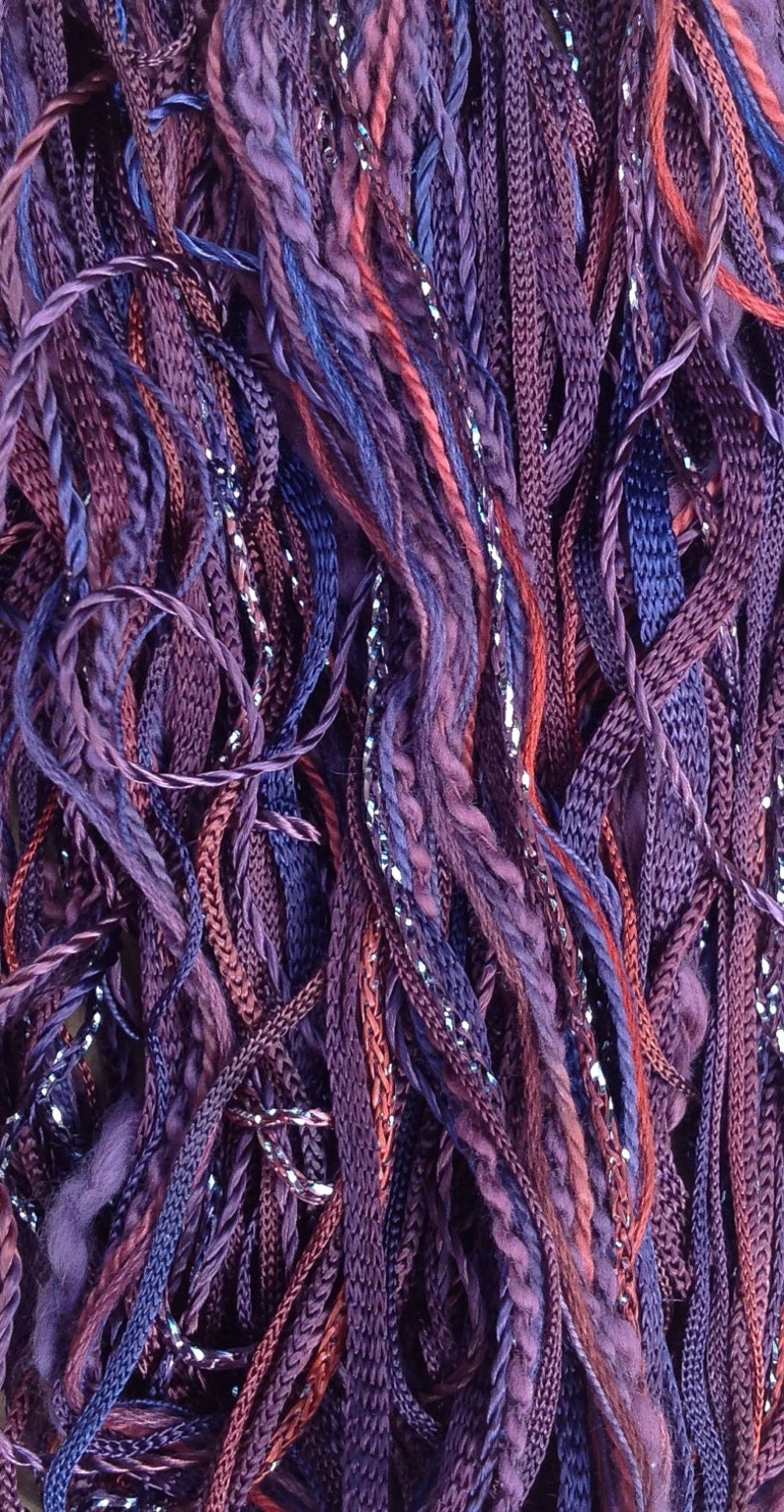 May include: A close-up of a bundle of purple, blue, and burgundy yarn with silver glitter thread woven throughout.