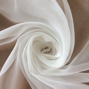 May include: White sheer fabric draped in a swirling pattern, creating a soft, delicate rose shape.