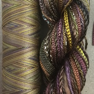 May include: Two spools of embroidery floss, one is a solid green and brown color, the other is a multi-colored mix of brown, green, purple, and gold with silver glitter.