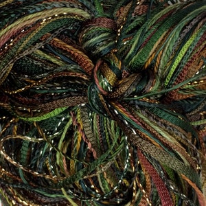May include: Close-up of a skein of yarn with a mix of green, brown, and gold threads. The yarn has a textured appearance with a variety of shades, including olive, forest, and bronze. The gold threads add a subtle shimmer to the yarn.