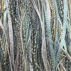 以下が含まれることがあります： 青、緑、茶色、金色の色合いの糸の束をクローズアップした写真です。糸はランダムなパターンで配置されており、質感があり視覚的に魅力的なディスプレイになっています。