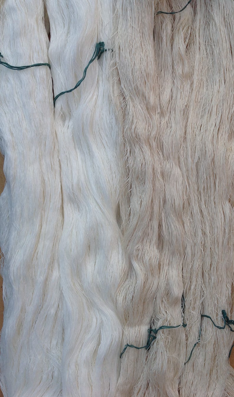 May include: Two bundles of white and off-white yarn tied together with green string. The yarn is soft and fluffy, and it appears to be made of natural fibers.