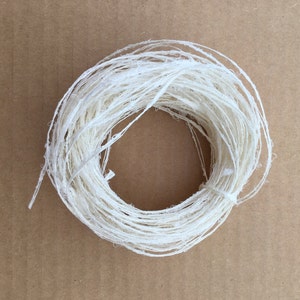 Può includere: Un filo bianco di fibra naturale, avvolto in un cerchio, su uno sfondo marrone.