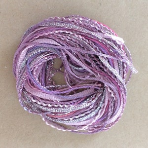 May include: A bundle of purple, pink, and silver embroidery floss. The floss is twisted and braided together.
