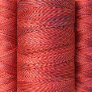 May include: Three spools of red and purple thread wound together. The thread is a variegated color with red and purple hues.