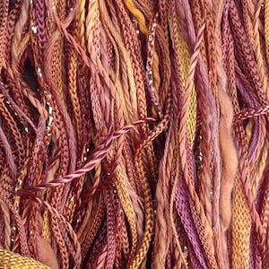Può includere: Primo piano di un insieme di filo da ricamo colorato in tonalità di marrone, arancione e viola. Il filo è disposto in uno schema casuale, creando una trama e una presentazione visivamente accattivante.