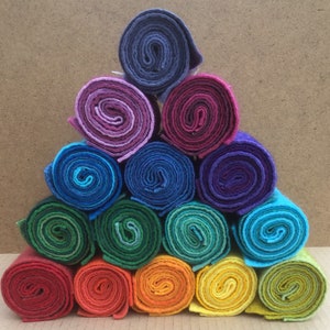 Könnte beinhalten: Eine Pyramide aus gerolltem Filzstoff in verschiedenen Farben, von tiefem Rot bis Violett. Jede Rolle ist eng gewickelt und zeigt die Textur des Stoffes. Die Anordnung erzeugt eine ansprechende Präsentation von Bastelmaterialien.