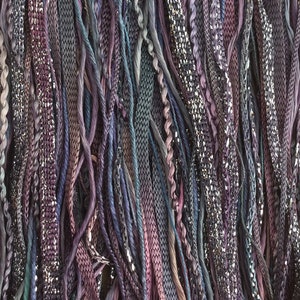 May include: A close-up of a variety of yarn strands in shades of purple, blue, and silver. The yarn is arranged in a vertical pattern, creating a textured and colorful background.