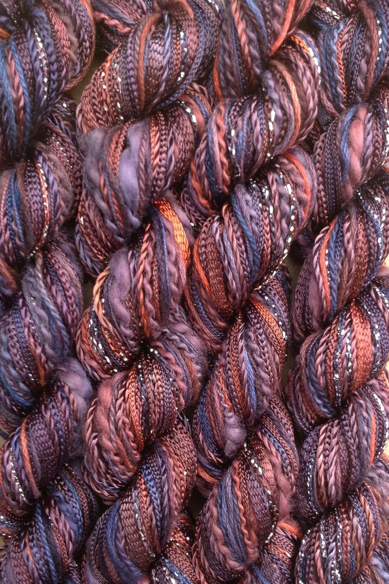 May include: Close-up of a bundle of yarn with a mix of purple, brown, and silver threads. The yarn is soft and fluffy, and it has a subtle sheen.