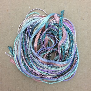 May include: A bundle of colorful embroidery floss in shades of teal, lavender, pink, and white. The floss is twisted and tangled together.