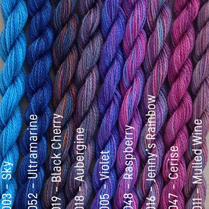 Puede incluir: Una colecci&oacute;n de ocho ovillos de hilo para bordar en tonos de azul, morado y rosa. El hilo est&aacute; dispuesto en una fila, con los colores pasando del azul al rosa. Los ovillos est&aacute;n etiquetados con n&uacute;meros y nombres, como "Sky", "Ultramarine", "Black Cherry", "Aubergine", "Violet", "Raspberry", "Jenny's Rainbow", "Cerise" y "Mulled Wine".