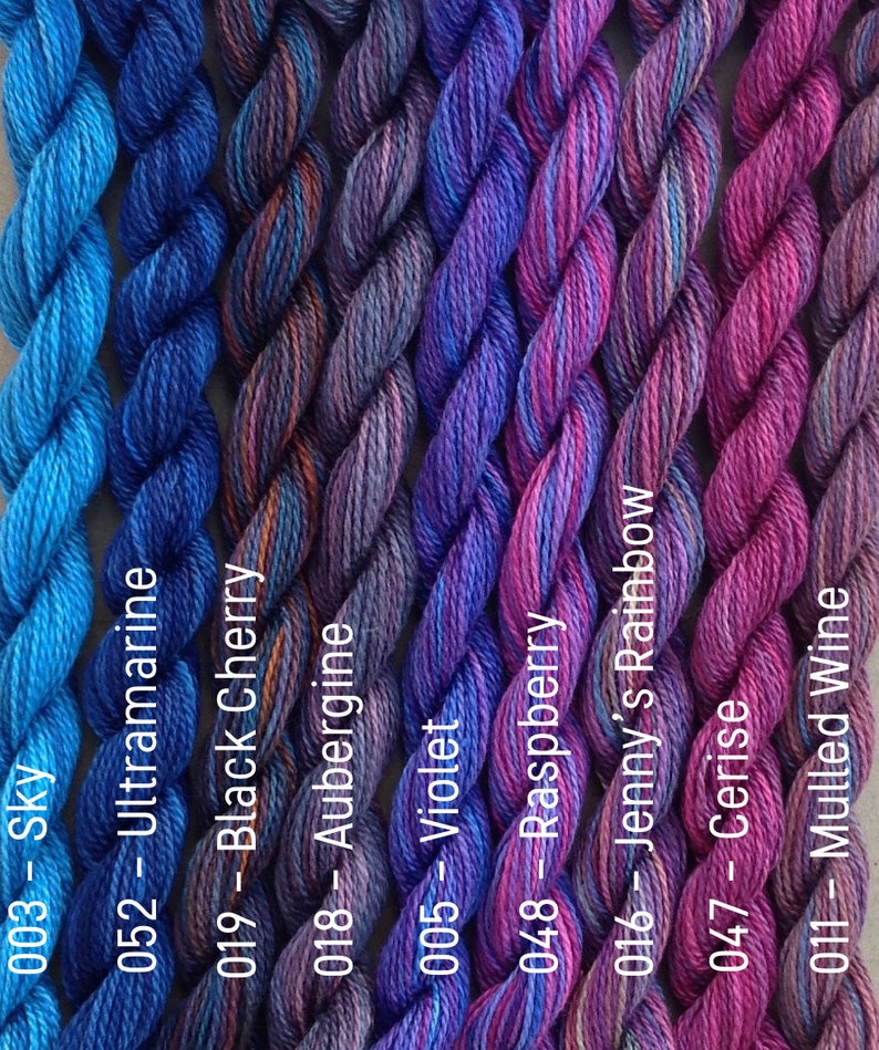 Puede incluir: Una colecci&oacute;n de ocho ovillos de hilo para bordar en tonos de azul, morado y rosa. El hilo est&aacute; dispuesto en una fila, con los colores pasando del azul al rosa. Los ovillos est&aacute;n etiquetados con n&uacute;meros y nombres, como "Sky", "Ultramarine", "Black Cherry", "Aubergine", "Violet", "Raspberry", "Jenny's Rainbow", "Cerise" y "Mulled Wine".