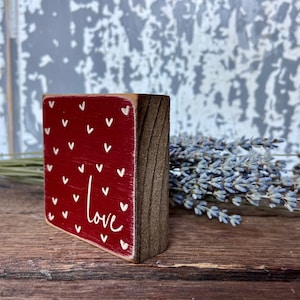 May include: A small wooden block with a red background and white hearts. The word "love" is written in white on the block.
