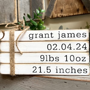 May include: White wooden sign with the text "grant james 02.04.24 9lbs 10oz 21.5 inches" in black lettering. The sign is tied with twine.