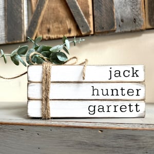May include: Three white wooden blocks stacked on top of each other. The blocks are tied together with twine. Each block has a name written on it: jack, hunter, garrett.