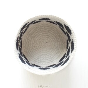 May include: A white crocheted bowl with a black painted design around the rim.
