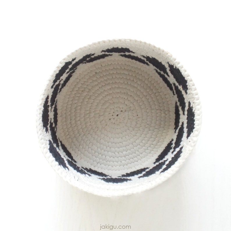 May include: A white crocheted bowl with a black painted design around the rim.