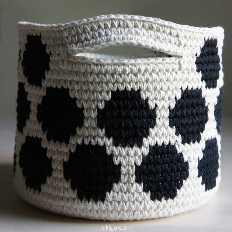 May include: A white crocheted basket with black polka dots. The basket has a handle and is made of a thick, textured yarn.