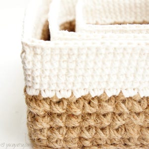 May include: Close-up of three handmade crochet baskets. The baskets are two-toned, with a natural brown jute base and a cream-coloured top. The baskets have a textured, woven appearance and are ideal for storage.