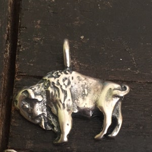 May include: A silver charm in the shape of a bison, with a detailed textured surface.