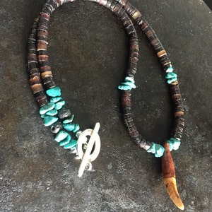 May include: A brown and turquoise beaded necklace with a tooth pendant. The necklace has a silver toggle clasp.