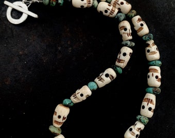 May include: A necklace featuring off-white carved skull beads alternating with small, irregular turquoise-colored stones. The strand is secured with a silver-toned metal toggle clasp consisting of a circular ring and a T-shaped bar.