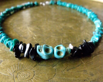 May include: A turquoise and black beaded necklace featuring two turquoise skull beads. The necklace is made of small, irregular turquoise and black beads, strung together with a silver clasp. The necklace is a unique piece of jewelry.