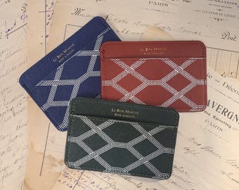 May include: Three rectangular card holders in blue, red, and dark green, each featuring a white geometric lattice pattern and the gold-stamped text "LE BON MARCHE RIVE GAUCHE" on the front. The card holders have a textured surface finish.