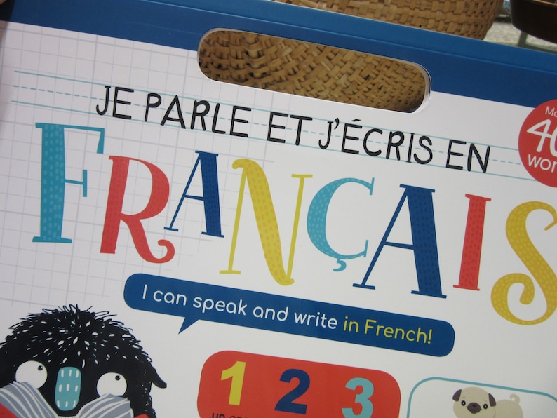 K&ouml;nnte beinhalten: Ein bunter Buchumschlag mit dem Titel "JE PARLE ET J'&Eacute;CRIS EN FRANCAIS" und dem Text "I can speak and write in French!" Der Umschlag zeigt eine Comicfigur mit gro&szlig;en Augen und einem blau-wei&szlig; gestreiften Schal.