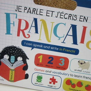 K&ouml;nnte beinhalten: Ein farbenfroher Buchumschlag mit dem Titel "Je parle et j'&eacute;cris en Fran&ccedil;ais", was "Ich spreche und schreibe Franz&ouml;sisch" bedeutet. Der Umschlag zeigt ein schwarzes Monster aus dem Cartoon, das ein Buch mit dem Wort "Fran&ccedil;ais" auf dem Umschlag liest. Das Buch enth&auml;lt auch die Zahlen 1, 2 und 3 in Franz&ouml;sisch und Englisch sowie Illustrationen eines Frosches, eines Puzzles und Erdbeeren.