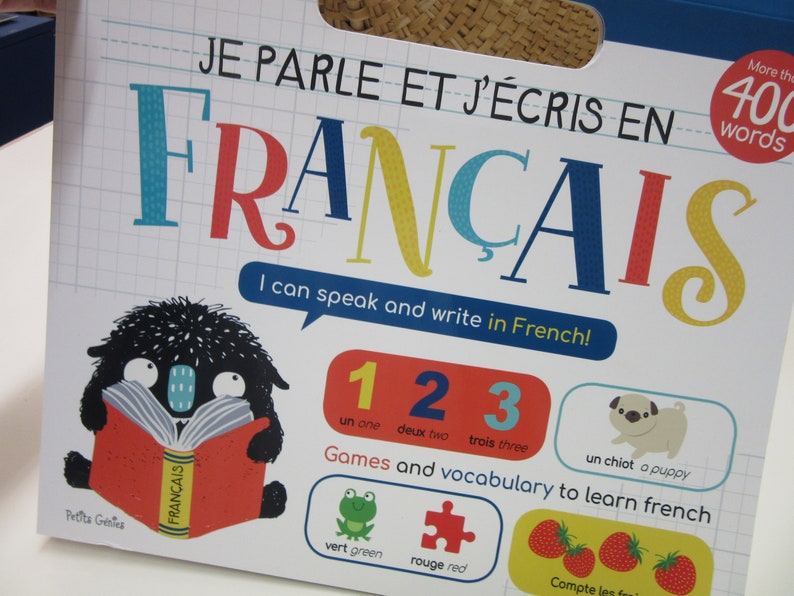 K&ouml;nnte beinhalten: Ein farbenfroher Buchumschlag mit dem Titel "Je parle et j'&eacute;cris en Fran&ccedil;ais", was "Ich spreche und schreibe Franz&ouml;sisch" bedeutet. Der Umschlag zeigt ein schwarzes Monster aus dem Cartoon, das ein Buch mit dem Wort "Fran&ccedil;ais" auf dem Umschlag liest. Das Buch enth&auml;lt auch die Zahlen 1, 2 und 3 in Franz&ouml;sisch und Englisch sowie Illustrationen eines Frosches, eines Puzzles und Erdbeeren.