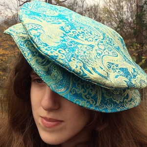 May include: A teal and gold patterned hat with a unique design. The hat is made of a soft, luxurious fabric and has a comfortable fit.
