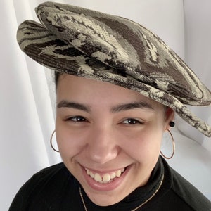 May include: A person wearing a brown and white patterned newsboy cap. The cap has a slightly curved brim and a pointed crown.