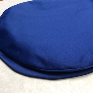 May include: A round, blue cushion with a smooth, satin-like fabric. The cushion has a thick, rolled edge.