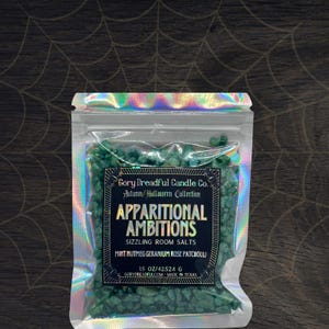 May include: A clear, iridescent bag filled with green room salts. The label reads "Gory Dreadful Candle Co. Autumn/Halloween Collection" and "Apparitional Ambitions." The bag contains 425.24 g of salts. The label also lists the scent as Mint, Nutmeg, Geranium, Rose, and Patchouli.