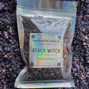 Könnte beinhalten: Ein transparenter Plastikbeutel gefüllt mit schwarzen und braunen Badesalzen. Der Beutel trägt ein Etikett mit der Aufschrift "Gory Dreadful Candle Co. Summer Collection Beach Witch Sizzling Room Salts Tropical Suntan Oil 6 oz/170.097 g GoryDreadful.com - Made in Texas"
