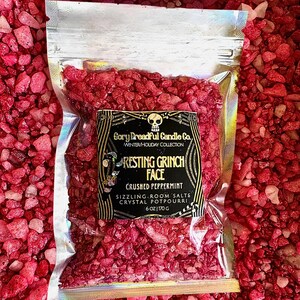 May include: A clear plastic bag filled with red and white crushed peppermint crystals. The bag has a black label with the text "Cory Dreadful Candle Co. Winter/Holiday Collection Resting Grinch Face Crushed Peppermint Sizzling Room Salts Crystal Potpourri 6 oz/170 g".