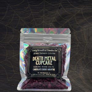 Peut inclure: Un sac holographique transparent contenant des sels de bain rouge foncé. L'étiquette indique "Death Metal Cupcake" avec le texte "Sizzling Room Salts Chocolate Cherry Absinthe." Le sac contient 425,24 grammes et provient de Gory Dreadful Candle Co.