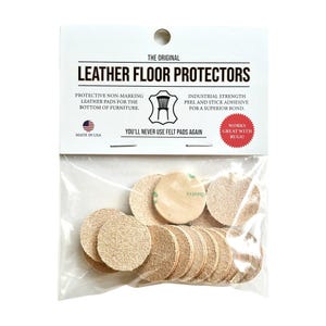 Puede incluir: Un paquete de protectores de suelo de cuero. El paquete incluye múltiples almohadillas circulares de color beige con respaldo adhesivo. El texto en el paquete dice "LEATHER FLOOR PROTECTORS" y "Protective non-marking leather pads for the bottom of furniture."