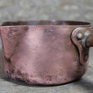 May include: A vintage copper saucepan with a handle. The saucepan has a worn, aged patina and is marked "Made in France".